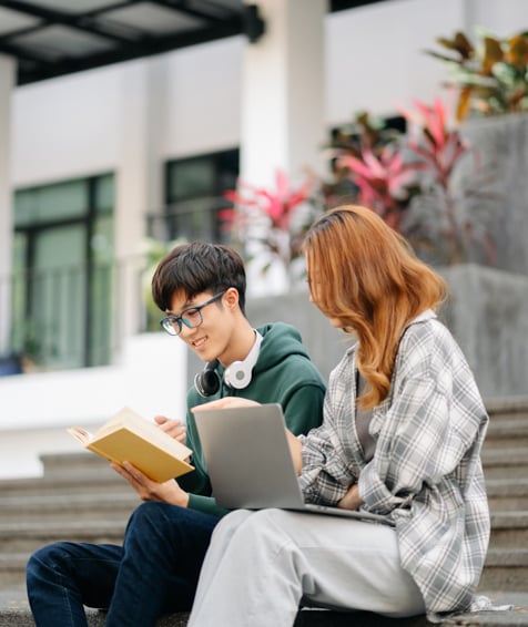 Two individuals looking at a laptop on university campus steps.